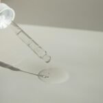 Close-up of a cosmetic pipette releasing serum onto a surface with soft sunlight.